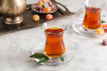 Glasses of Turkish tea with delights and leaves on light background