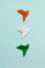 Three paper origami pigeons orange, white, and green on light blue vertical background