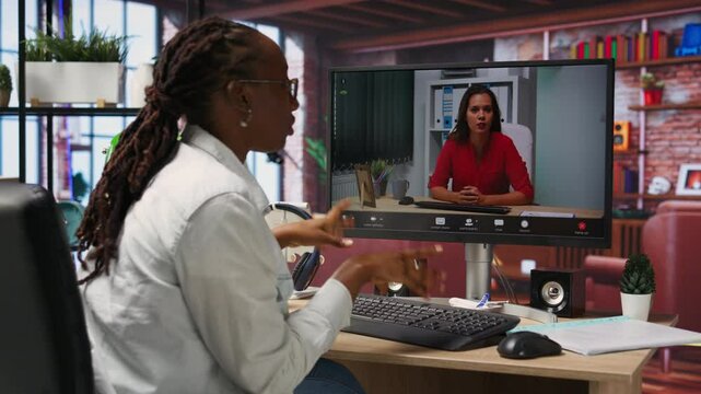 Remote employee in teleconference meeting with manager, answering inquiries. Friendly freelancer in home office sitting at desk in front of computer screen, greeting supervisor in videocall, camera B