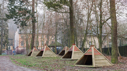 A group of five children's houses in the form of wooden pyramids on the playground.
