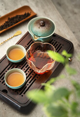 Still life photo of ceramic Gaiwan, clear glass pitcher, tea cups with fresh brewed dark oolong tea on tray in ceremony room. Soft light evokeing calming mindful tradition Chenese atmosphere.