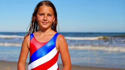 Smiling girl wearing a USA flag colored swimsuit poses on the beach with the ocean in the background - Powered by Adobe