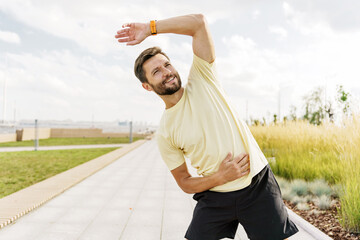 Man performs a stretching exercise in a park during a sunny day surrounded by greenery and pathways