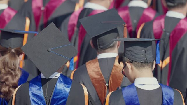 A group of graduates are standing in a row, all wearing black and blue graduation gowns. The graduates are wearing their caps and gowns, and they are all looking at the camera. Scene is one of pride