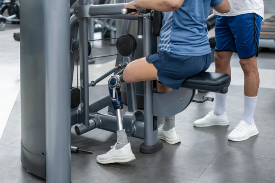 A female person with prosthetic leg doing fitness exercise equipment with a personal trainer