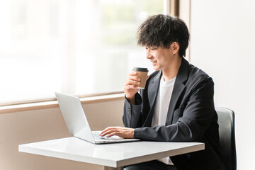 カフェ・シェアオフィスでパソコンを使って仕事するビジネスマン・男性
