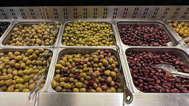 Assorted green and black olives in metal trays at a deli