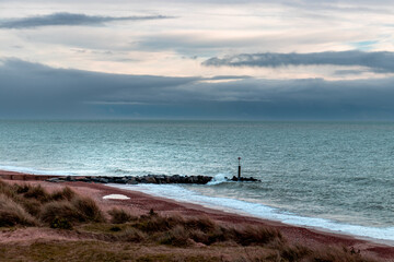 A tranquil view of Southbourne Beach featuring soft waves, grassy dunes, and a cloudy sky. Perfect for relaxation and nature lovers