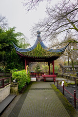 A picturesque Asian-style pavilion with a green-tiled roof surrounded by lush greenery in a tranquil garden.