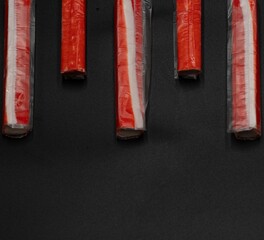 Crab sticks on a black background with space for text laid out in a row © Olha