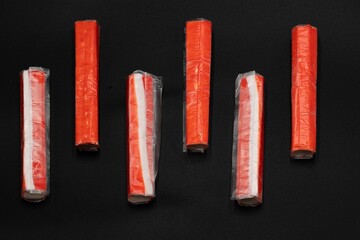 Crab sticks on a black background with space for text laid out in a row © Olha