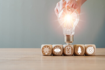 A glowing light bulb atop wooden blocks with icons, representing creativity, innovation, and...