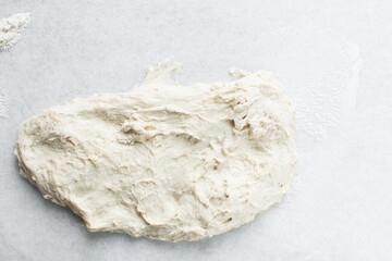Overhead view of high hydration dough being shaped on a white granite countertop, top view of homemade bread dough on white countertop, process of making artisan bread