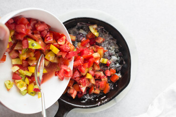Overhead view of diced tomatoes and onions in a cast iron skillet, top view of chopped tomatoes and onion being fried in a skillet, process of making shakshuka