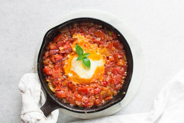Overhead view of shakshuka in a cast iron skillet, top view of toast and egg poached in tomato sauce, shakshuka with well done eggs