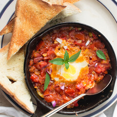 Overhead view of shakshuka in a cast iron skillet and toast, top view of toast and egg poached in tomato sauce, bread and  shakshuka with well done eggs