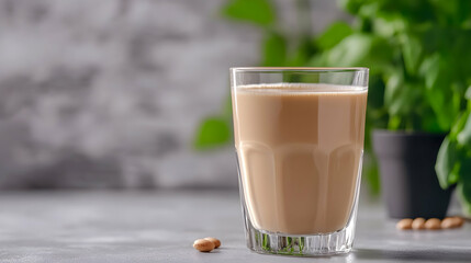 Soy milk in glass, kitchen counter, plant background; healthy drink recipe