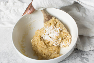 mixing flour into vanilla cookie dough in a white mixing bowl, plain vanilla cookie dough about to...
