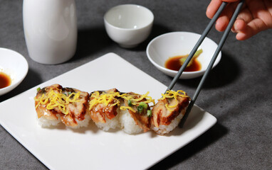Eel sushi with egg garnish on top. Pick up sushi with chopsticks. 
