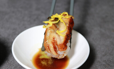 Eel sushi with egg garnish on top. Pick up sushi with chopsticks. 
