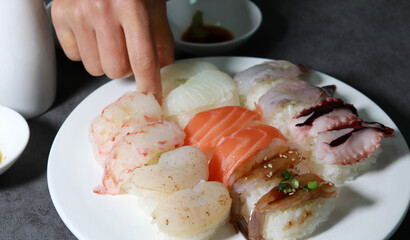 Various sushi on a white plate. Pick up sushi with one's fingers. 
