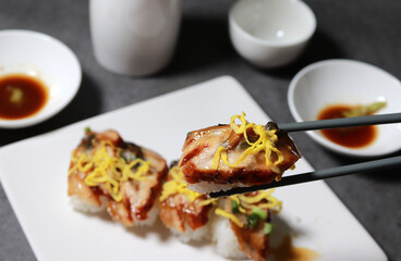 Eel sushi with egg garnish on top. Pick up sushi with chopsticks. 

