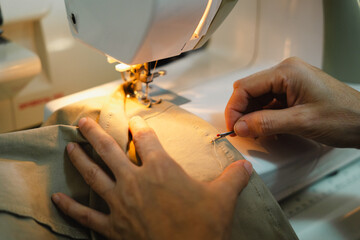 Woman hands using seam ripper tool to unstitch the thread while sewing light brown fabric with...