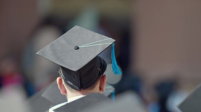 A man wearing a black cap and gown is standing in front of a building. He is wearing a graduation cap and gown, which suggests that he has recently graduated from college