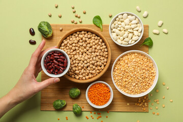 Beans in bowls and female hand on green background, top view