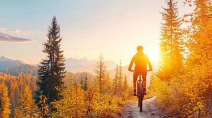 Fototapeta premium A cyclist rides through a vibrant forest trail at sunset, surrounded by golden foliage and majestic mountains in the background.