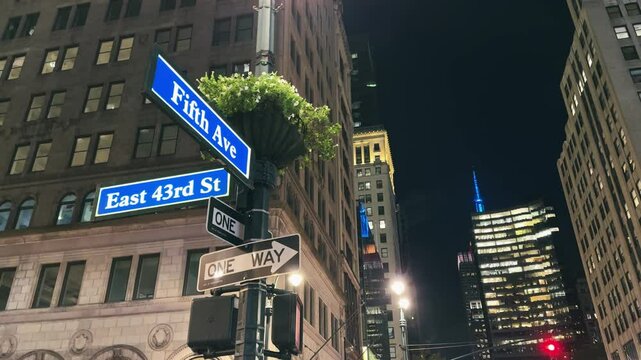 New York scene at night with Fifth Avenue and East 43rd street illuminated sign on street crossroad with illuminated office building windows at background