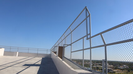 Rooftop wire mesh fence. Wire mesh fence posts and fences on high rise building rooftop for safety and security on low angle view building background and sky with copy space. Selective focus