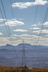 Power lines stretching across rugged mountains and forests under a bright sky in Tasmania, Australia