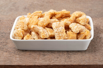 Fried pork rinds in a white ceramic plate on a brown wooden table.