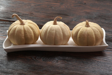Whole uncooked decorative pumpkins in a row on a white dish with a wooden background. Autumn...