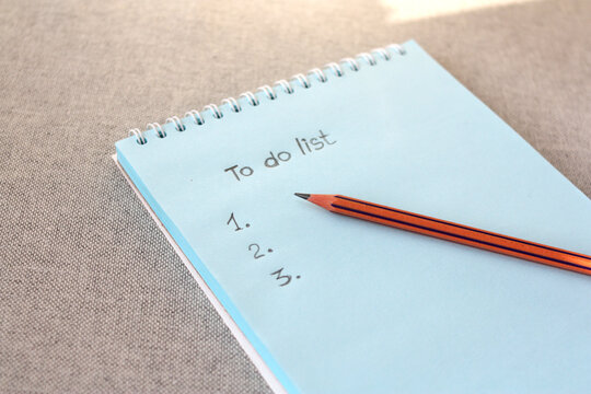 Notebook and pencil with to-do list numbers against a gray background. A to-do list on a blank sheet of paper.