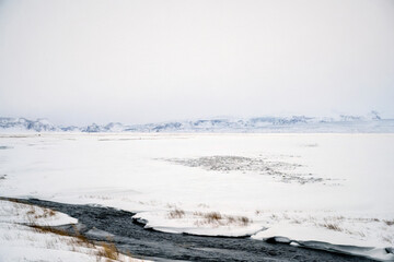 Landscape view of river flow with snow covered fields and mountain ranges in Iceland. Nature, travel, winter background, or wallpaper © Leo Lintang