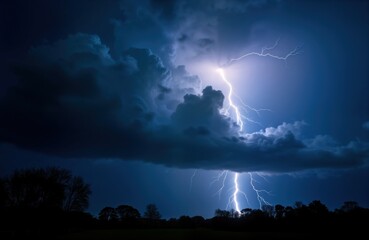 Dramatic nighttime sky shows powerful lightning bolt illuminating dark clouds. Stormy weather scene with dark silhouettes of trees, field below. Intense natural energy. Photo captures dramatic
