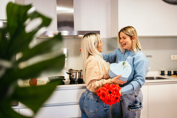 Two happy women exchanging gifts and flowers in a modern kitchen on valentine's day