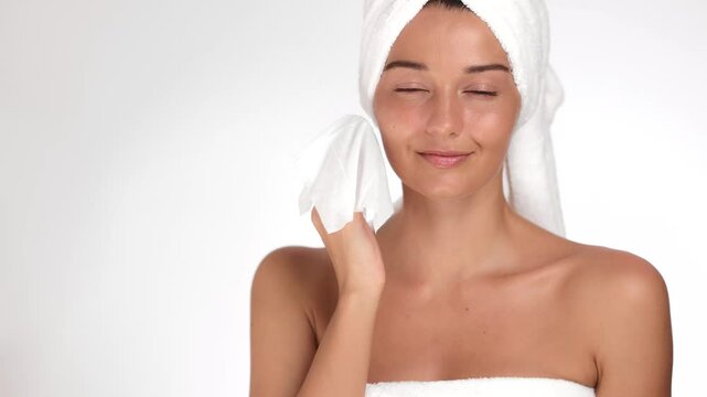 Cheerful woman with a towel turban gently patting her face dry after a skincare session. Ideal for advertising beauty, wellness, and self-care products highlighting radiant, healthy skin. 