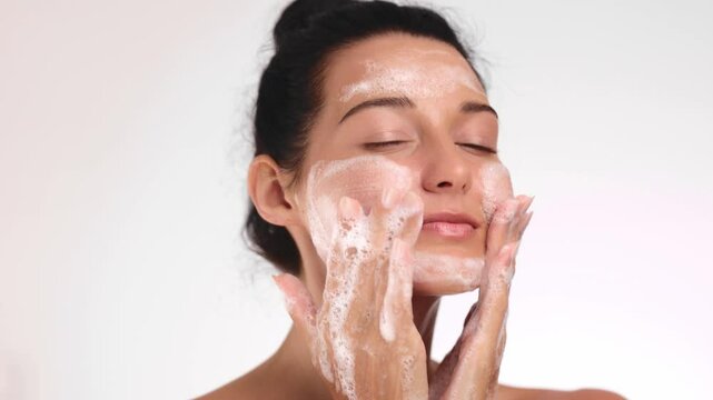 Radiant woman cleansing her face with a foamy cleanser, smiling during her skincare routine. Ideal for advertising beauty, wellness, or self-care products promoting healthy skin. 