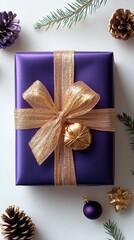 A beautifully wrapped purple gift adorned with a gold ribbon and bow, surrounded by pine cones and holiday decorations.