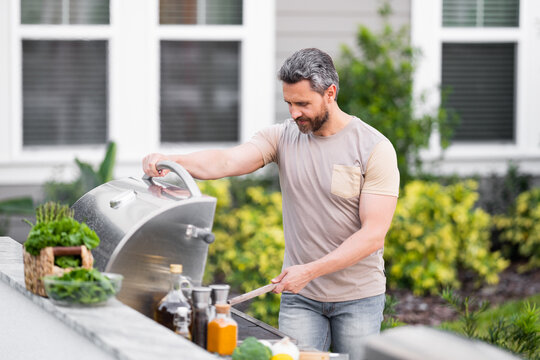 Handsome man barbecue on a grill at backyard. Cooking outdoors and american lifestyle concept. Handsome man preparing barbecue meat. Concept of eating and cooking outdoor.