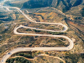 A winding asphalt road that passes through areas with few trees in autumn. An S-curved highway