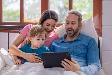 Family enjoying a cozy morning together while watching a tablet in bed