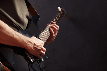 Posing hands of rock guitarist playing the black guitar on dark stage.