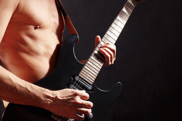 Artist playing chord on black guitar on dark stage.