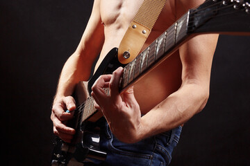 Artist playing chord on guitar on dark stage.
