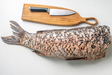 Gutted carp fish, headless on a white table with a cutting board and a knife.