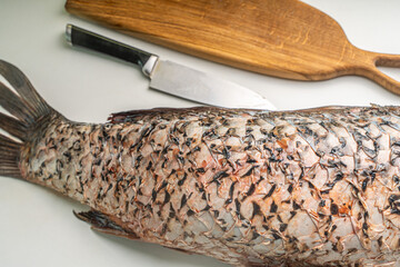Gutted carp fish, headless on a white table with a cutting board and a knife.